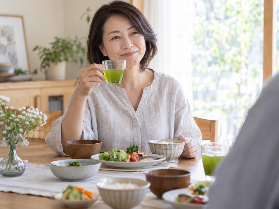 自宅の食卓で食事と緑茶を楽しむ50代の女性